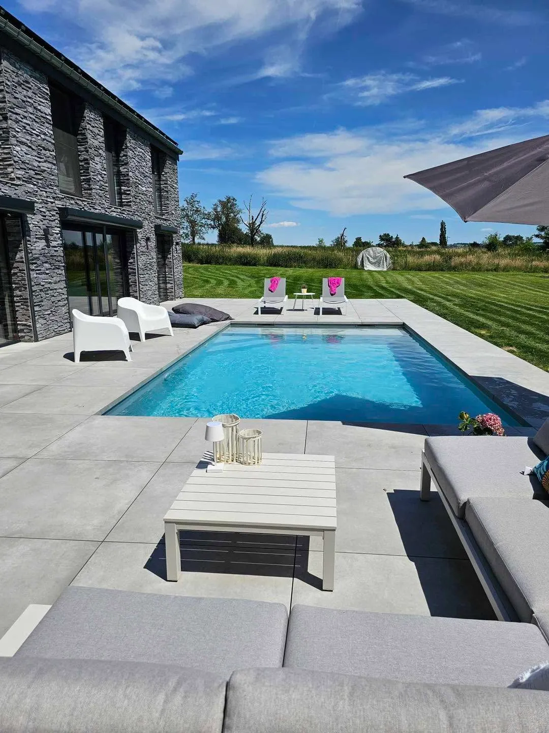 Piscine rectangulaire entourée d’une grande terrasse claire et d’un jardin