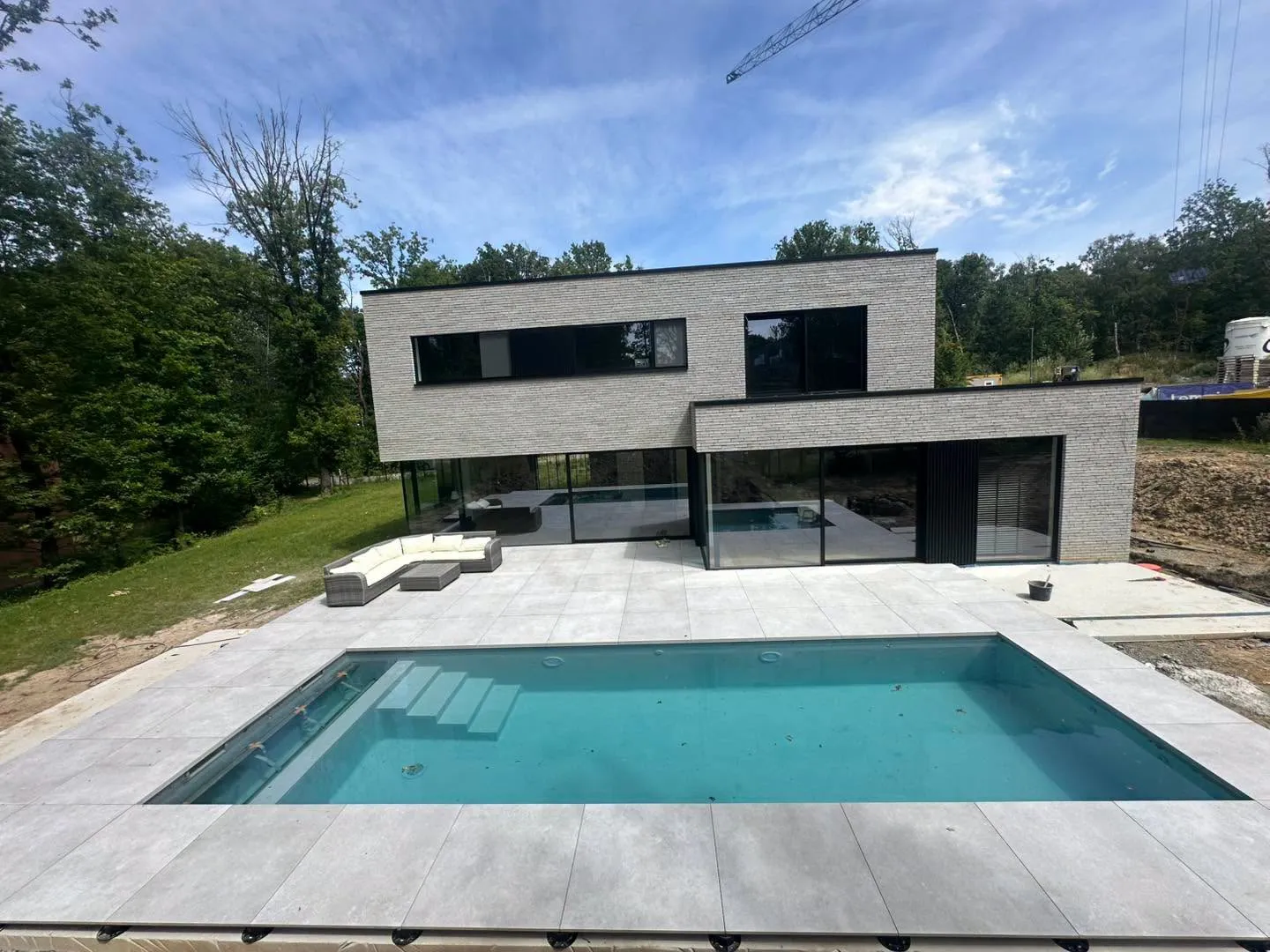 Piscine contemporaine et terrasse claire devant une maison moderne