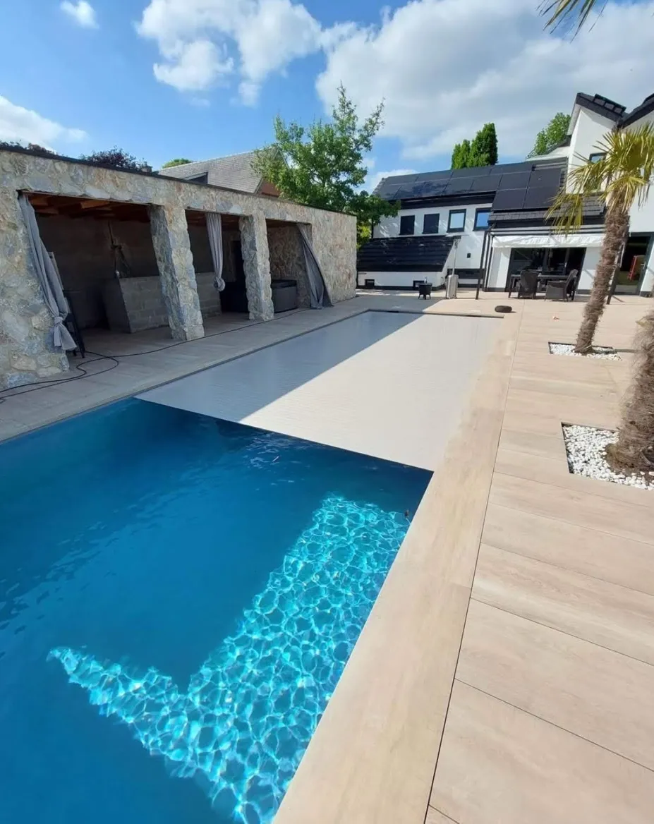 Piscine avec volet partiellement fermé, terrasse claire et palmiers