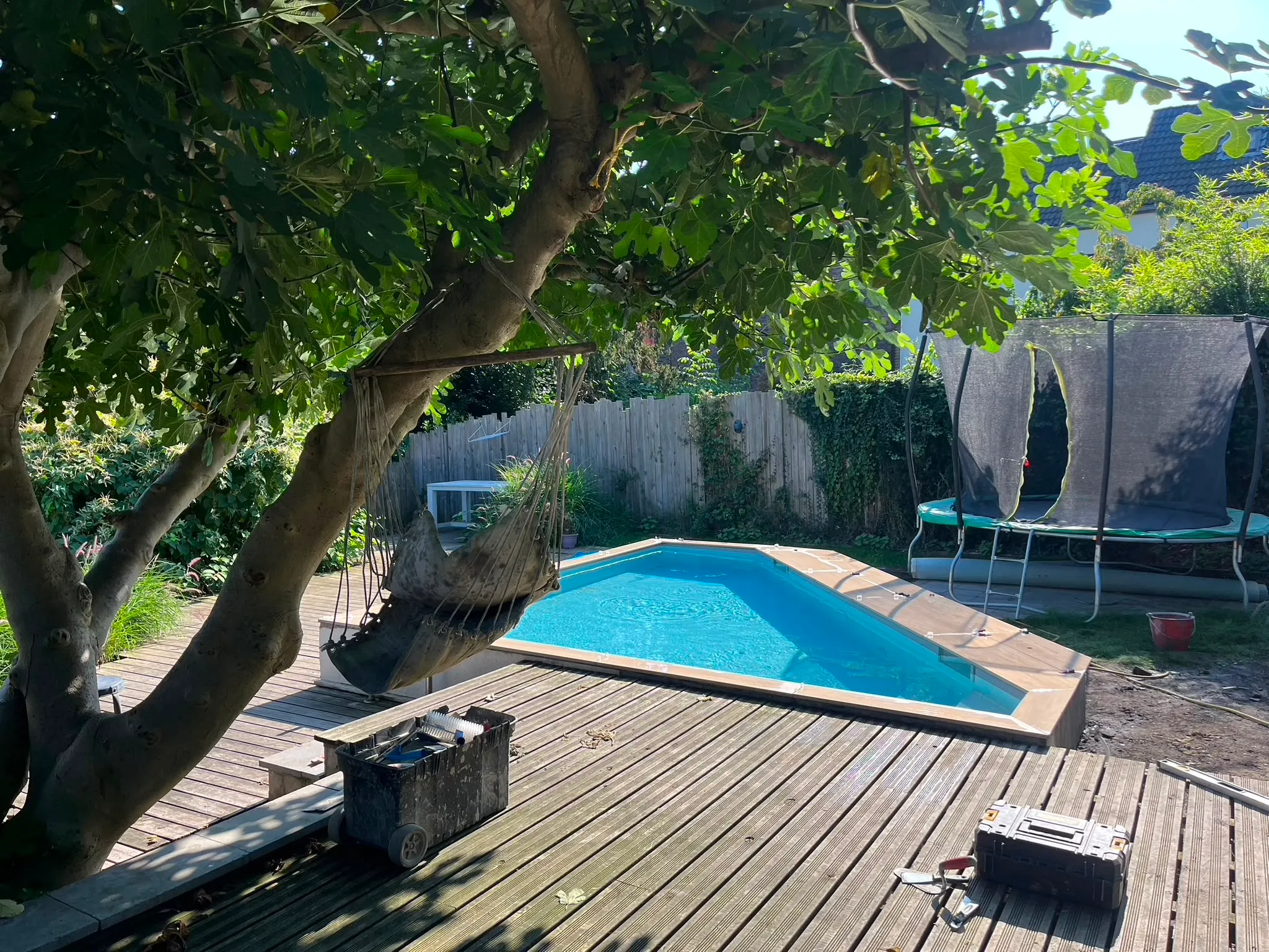 Petit bassin extérieur intégré dans une terrasse en bois sous un grand arbre
