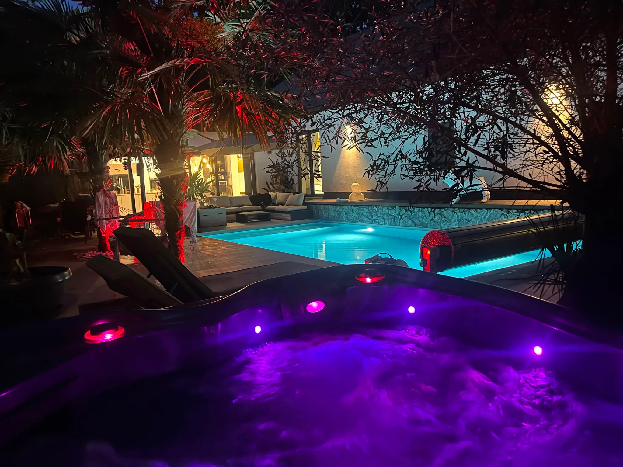 Piscine éclairée de nuit dans un jardin avec spa au premier plan