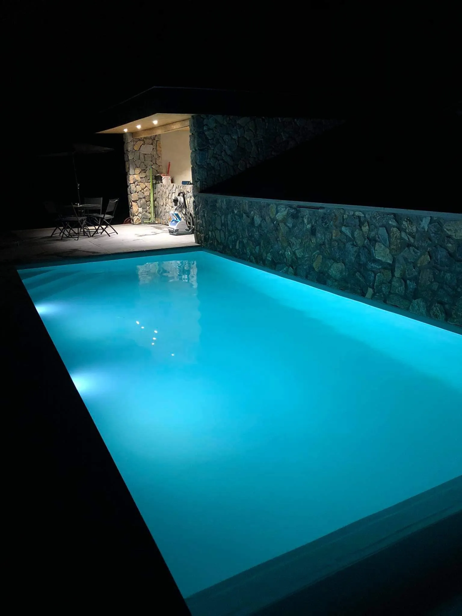 Piscine éclairée de nuit bordée d’un mur en pierre