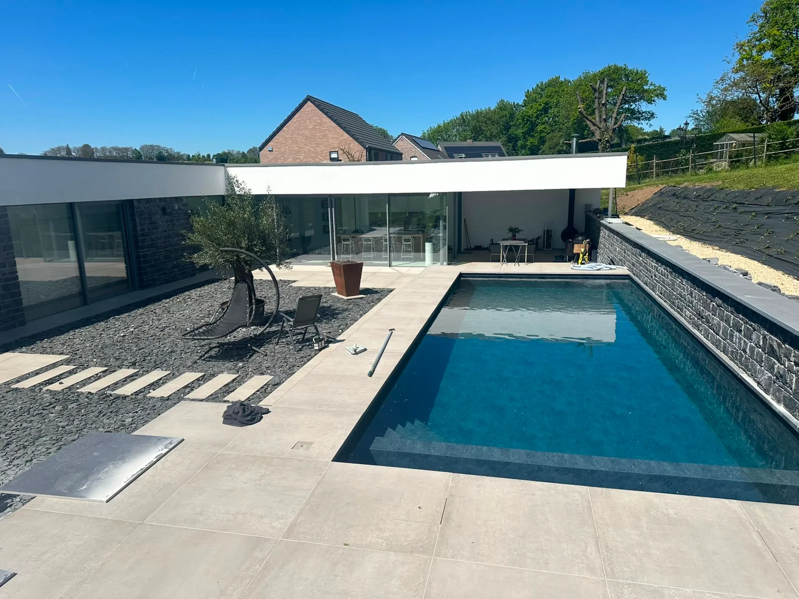 Piscine contemporaine bordée d’un mur en pierre et d’une terrasse claire