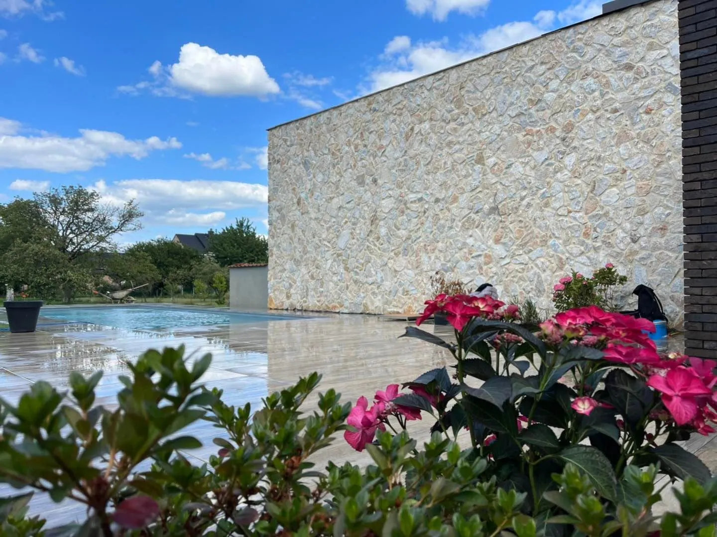 Mur en pierre, terrasse claire et végétation au bord d’une piscine