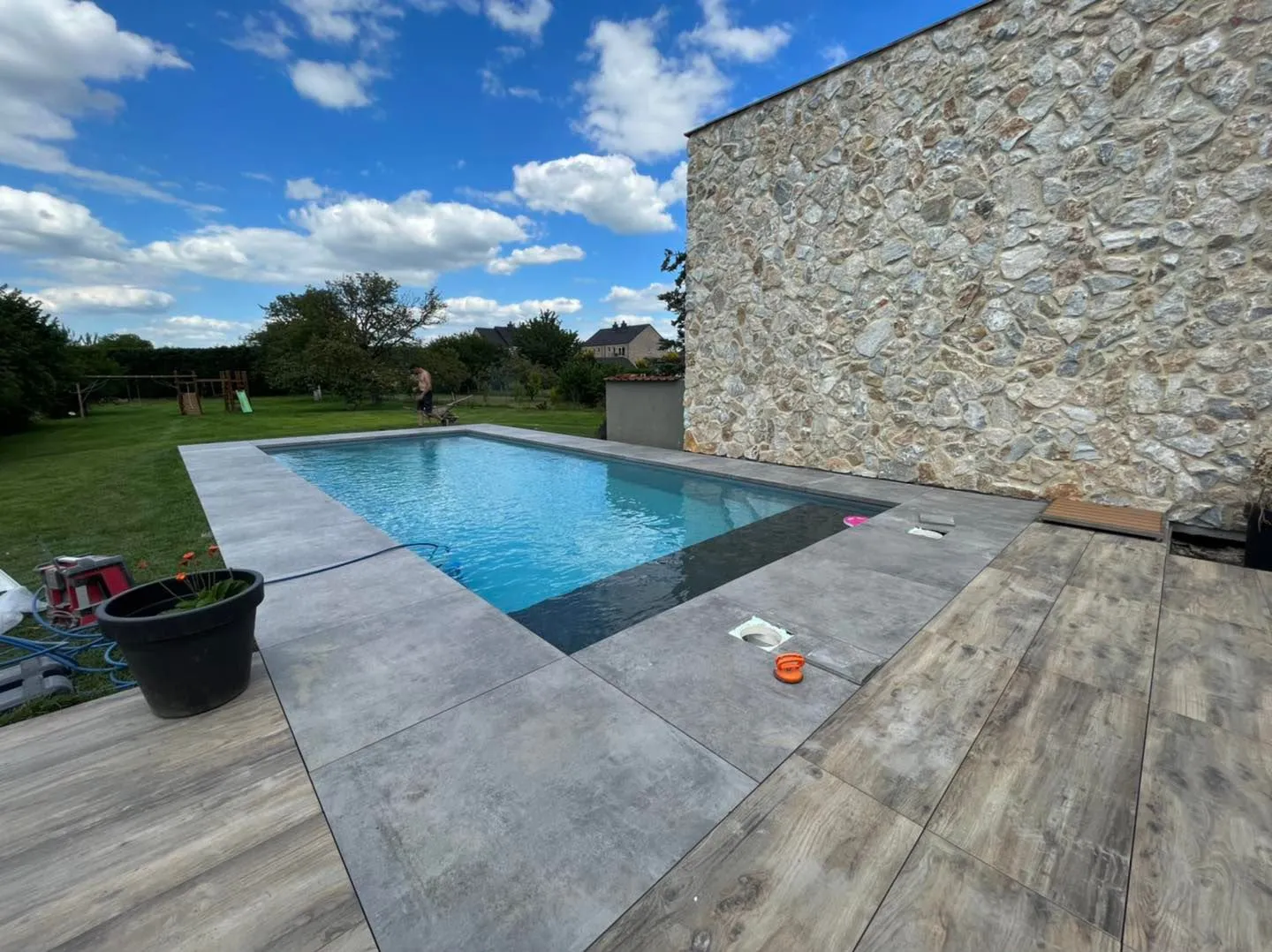 Piscine bordée d’une grande paroi en pierre et d’une terrasse minérale