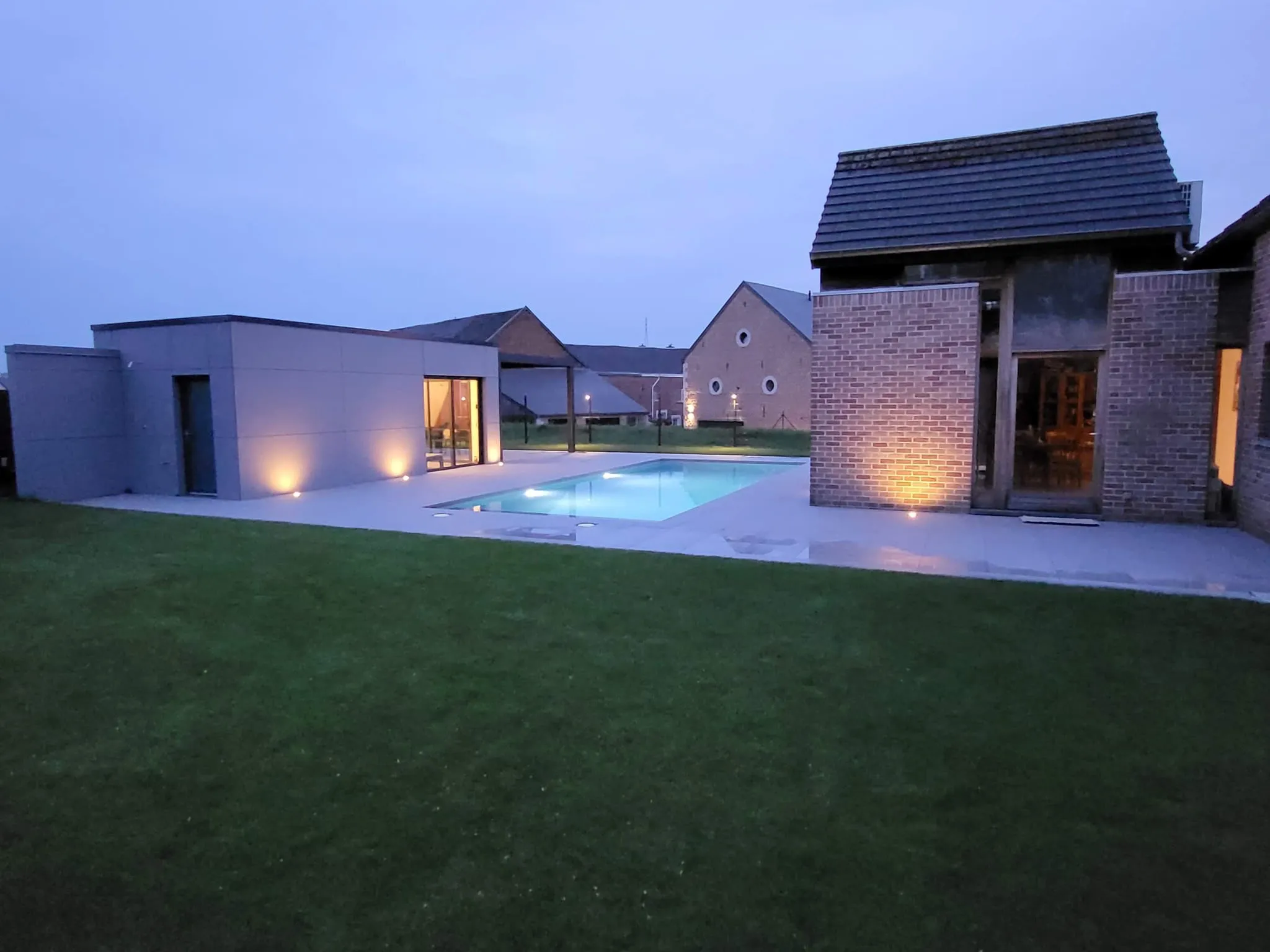 Piscine contemporaine éclairée au crépuscule dans un grand jardin