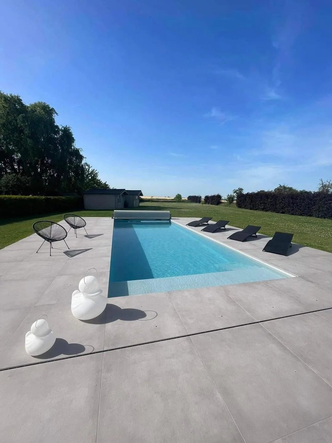 Piscine rectangulaire avec plage immergée, terrasse claire et vaste jardin ouvert