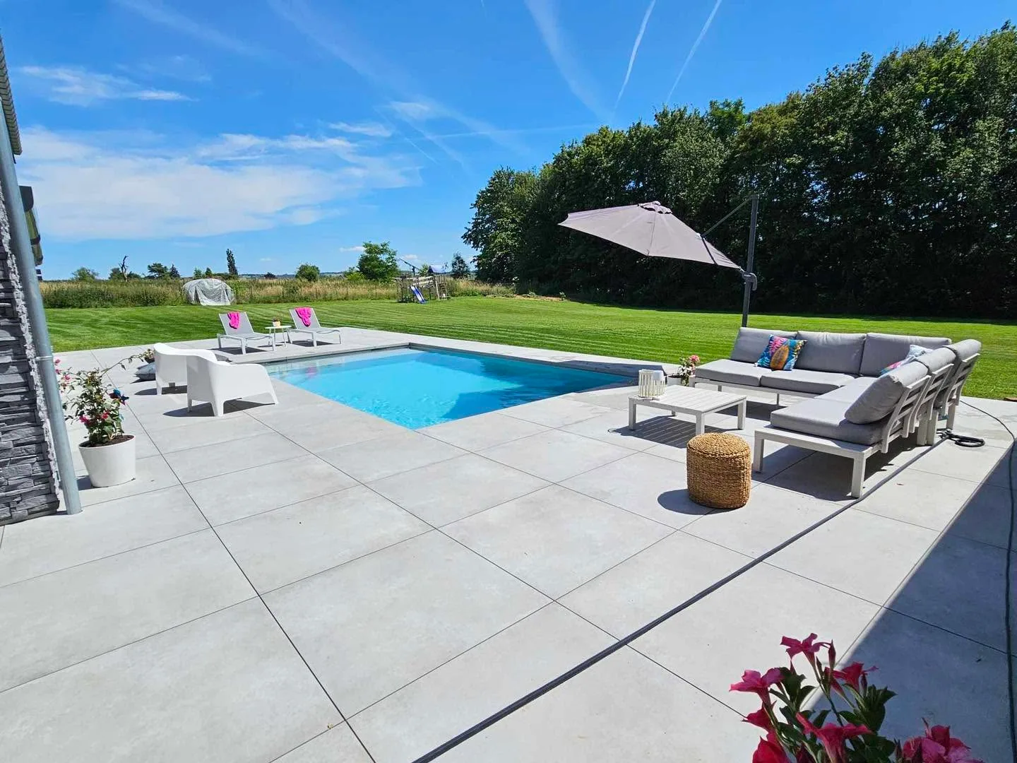 Piscine contemporaine intégrée à une grande terrasse meublée dans un jardin